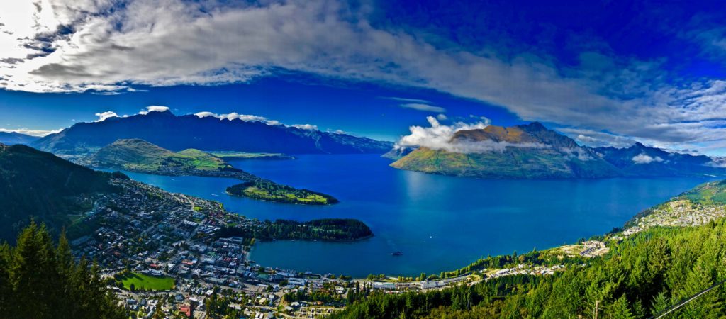 image of a lake bounded by mountainous terrain. There is a village in the foreground at the base of the mountains and shore of the lake.
