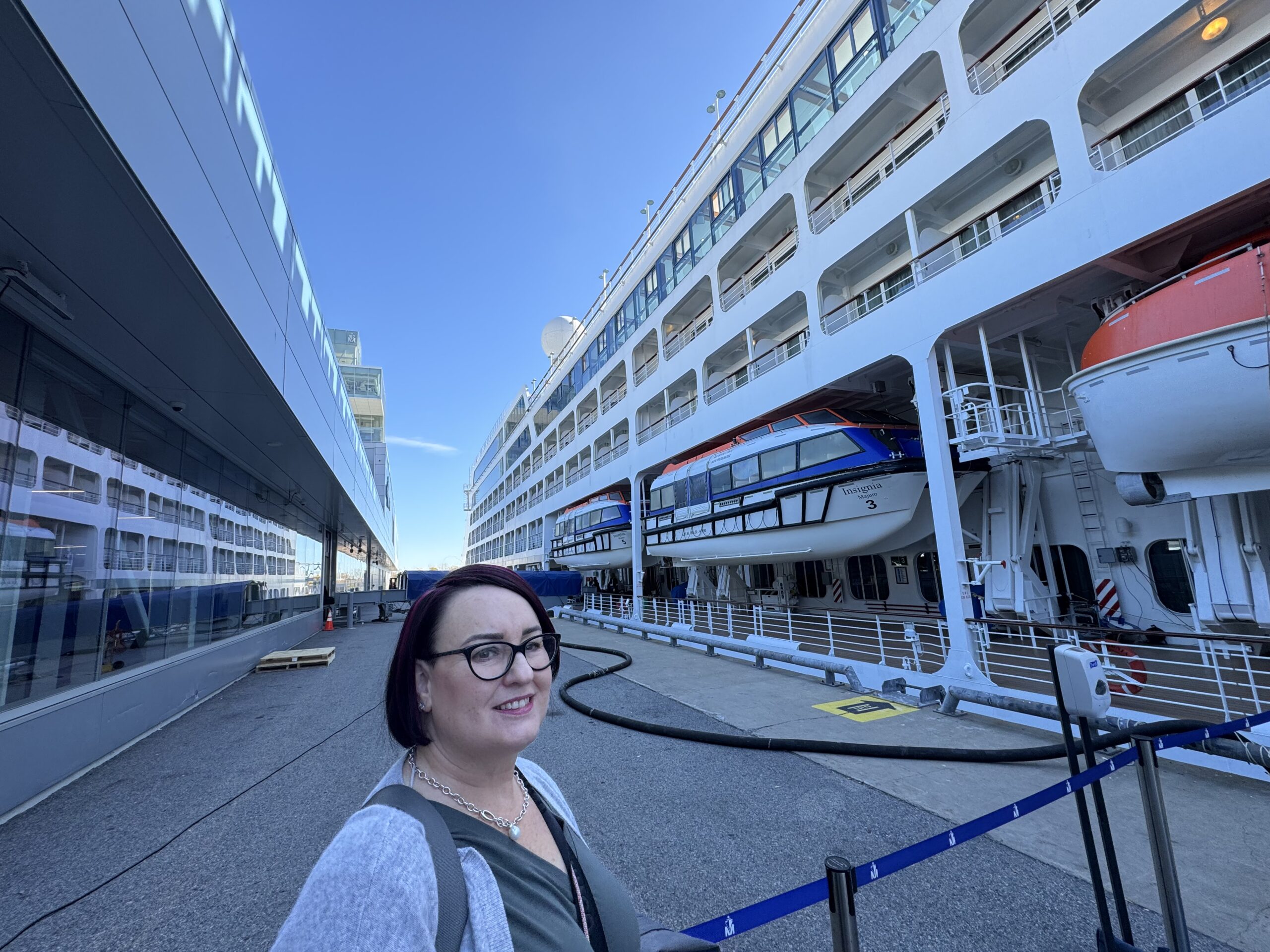 Mardi in front of of our ship. The ship is white and looms large behind her with multiple decksn and a number of life boats lining one deck.