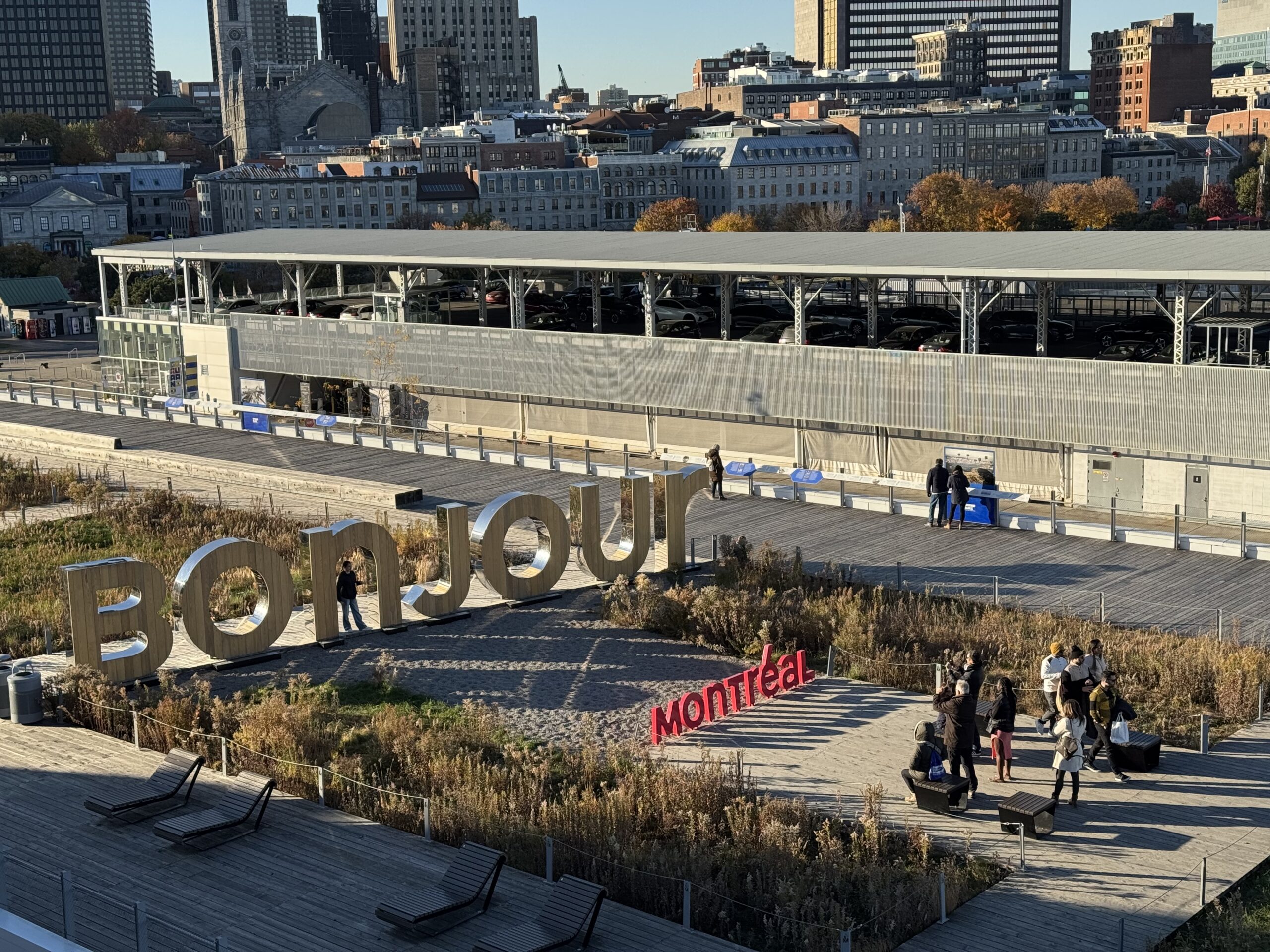 A sign that’s says bonjour Montreal. The letters are large three d shapes set on the crowd. People mill around taking photos among the letters.
