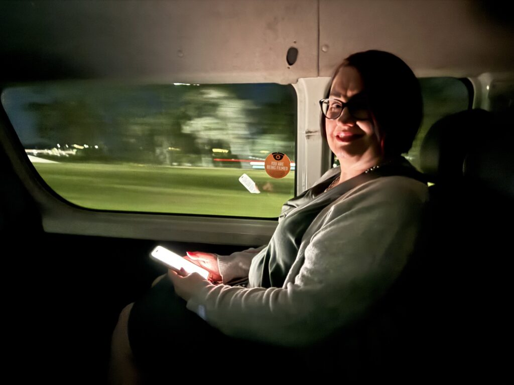 Mardi in the cab on the way to the airport, the glow from her phone eliminate her face she’s smiling excited for the tripahead