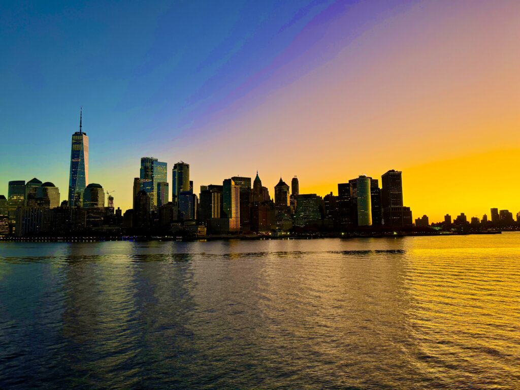 The golden and blue sky of sunrise over New York from the Hudson River. The world trade centre, left, dominates the skyline. The remaining building of the lower end of manhattan are silohetted.
