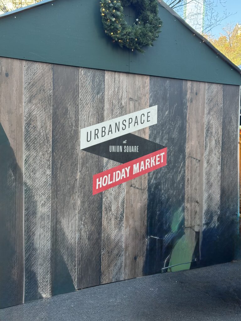 The entry to the markets. A wooden wall, sign says urban space. Union square. Holiday market.